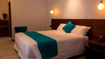 A neatly made bed with a teal throw, a wooden headboard, and bedside tables with lamps.