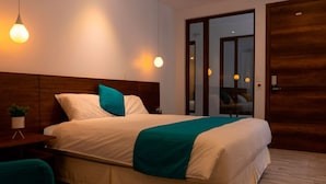 A modern hotel room with a large bed, a wooden headboard, a small table with a plant, and a view through a glass door. - REEC Latacunga by Oro Verde Hotels (Latacunga)