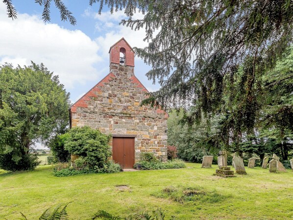 A stone church with a bell tower, surrounded by a cemetery with headstones. - 2 bedroom accommodation in Panton (Panton)