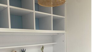 Ein Schlafzimmer mit einem weißen Bett, einer weißen Regaleinrichtung mit Dekorationen und einer gewobenen Leuchte.
