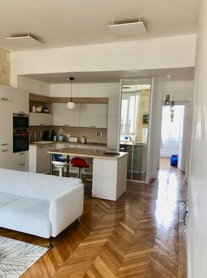 Une cuisine moderne avec des meubles blancs, un îlot central et un coin repas comprenant un canapé blanc et des chaises rouges.