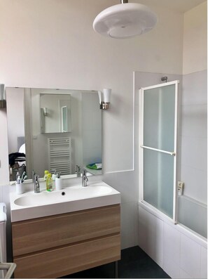 Une salle de bain moderne avec un grand lavabo, un miroir, un porte-serviettes et une porte de douche en verre dépoli.