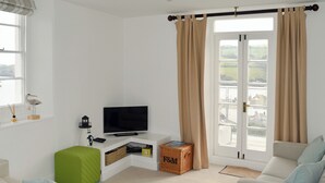 Een moderne woonkamer met een flatscreen televisie, een groene ottoman en een rieten mand.