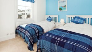 Een slaapkamer met twee bedden, een raam met uitzicht op gebouwen, een blauwe wand en een lijst met een afbeelding aan de wand.