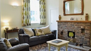 A living room with a sofa, a small table, a fireplace, and a window with curtains. - 3 bedroom accommodation in Rudston, near Bridlington (Rudston, near Bridlington)