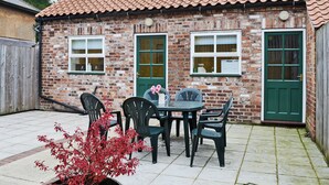 A brick building with a tiled roof, two windows, a green door, and a patio with a table and chairs. - 3 bedroom accommodation in Rudston, near Bridlington (Rudston, near Bridlington)