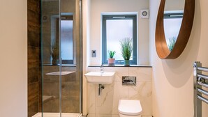 A modern bathroom with a glass-enclosed shower, a sink, and a toilet. There is a window with plants on the windowsill and a wooden-framed mirror on the wall. - Bootham Row Hideaway -  a couples retreat that sleeps 2 guests  in 1 studio (York)