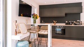 A modern kitchen with dark cabinets, a flat-screen TV, and a dining area with wicker chairs and a small table. - Bootham Row Hideaway -  a couples retreat that sleeps 2 guests  in 1 studio (York)