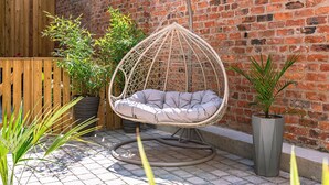 A wicker hanging chair with a cushion, a brick wall, and potted plants. - Bootham Row Hideaway -  a couples retreat that sleeps 2 guests  in 1 studio (York)