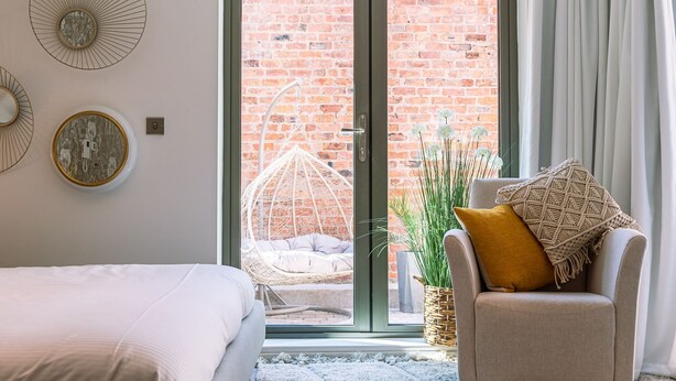 A bedroom with a bed, a chair, a hanging chair, and a view of a brick wall through a glass door. - Bootham Row Hideaway -  a couples retreat that sleeps 2 guests  in 1 studio (York)