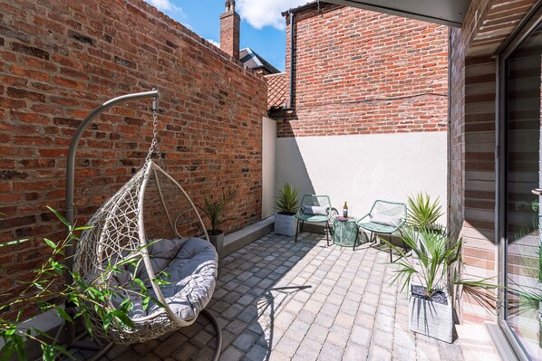 A patio with a hanging chair, two chairs, and potted plants.