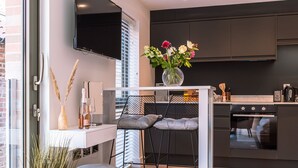 Eine moderne Küche mit schwarzem Arbeitsplatz, einem eingebauten Backofen und einem Essbereich mit zwei schwarzen Stühlen und einem weißen Tisch.