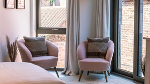 Ein Schlafzimmer mit zwei Sesseln, einem Bett und einem großen Fenster mit Vorhängen.