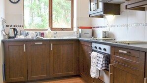 Une cuisine avec des meubles de rangement en bois, une cuisinière, un évier et une fenêtre donnant sur des arbres.