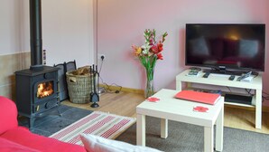 Un salon avec une cheminée, un téléviseur, une table blanche et un vase de fleurs.