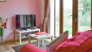 Un salon comprenant un téléviseur, une table basse blanche, un canapé rouge et une porte vitrée donnant sur un jardin.