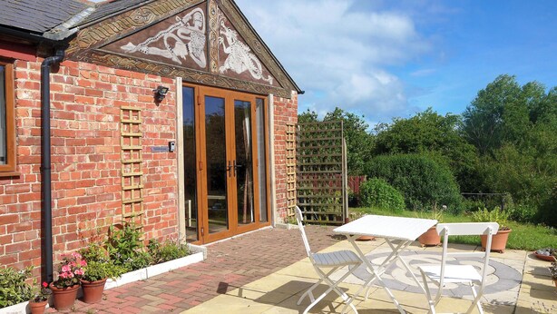 Un bâtiment en briques avec une grande porte vitrée, un patio avec une table et des chaises, et des plantes en pot.