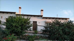 A building with a stone wall, a wooden gate, and a garden with red flowers. - Apartamentos en plena naturaleza El Elanio Azul. (Arcos de la Frontera)