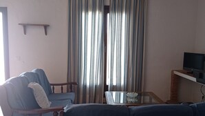 A living room with a sofa, a chair, a coffee table, and curtains. - Apartamentos en plena naturaleza El Elanio Azul. (Arcos de la Frontera)