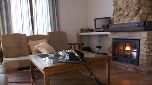 A living room with a stone fireplace, a sofa, and a television on a shelf. - Apartamentos en plena naturaleza El Elanio Azul. (Arcos de la Frontera)