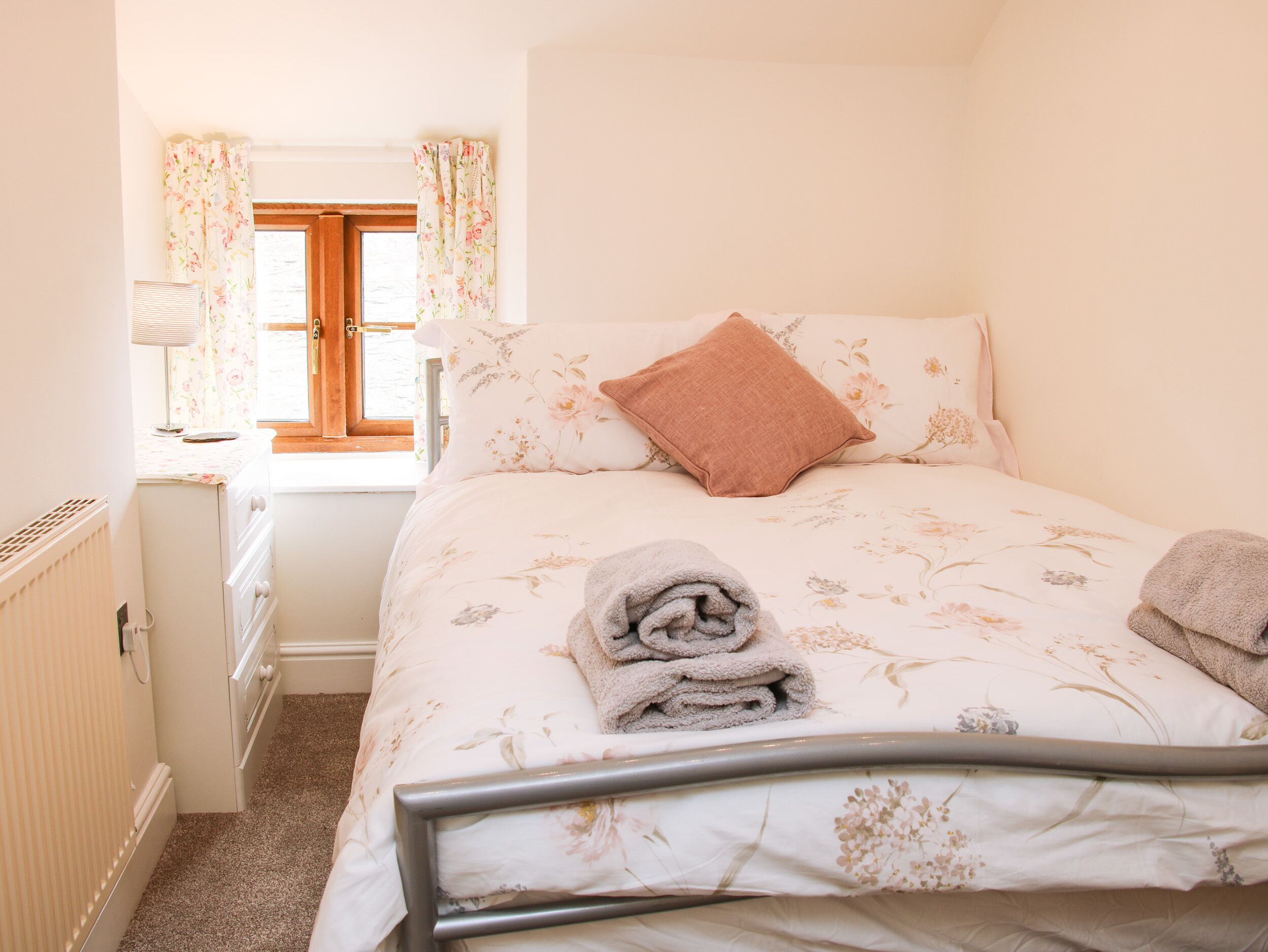 A bedroom with a bed, a window with curtains, a radiator, and a lamp.