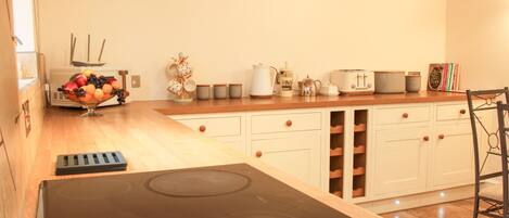 A kitchen with a black stove, wooden cabinets, and a countertop with various appliances and a fruit bowl.