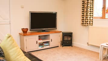 A living room with a television on a wooden stand, a white cabinet with books, a black leather sofa, and a black wood-burning stove.