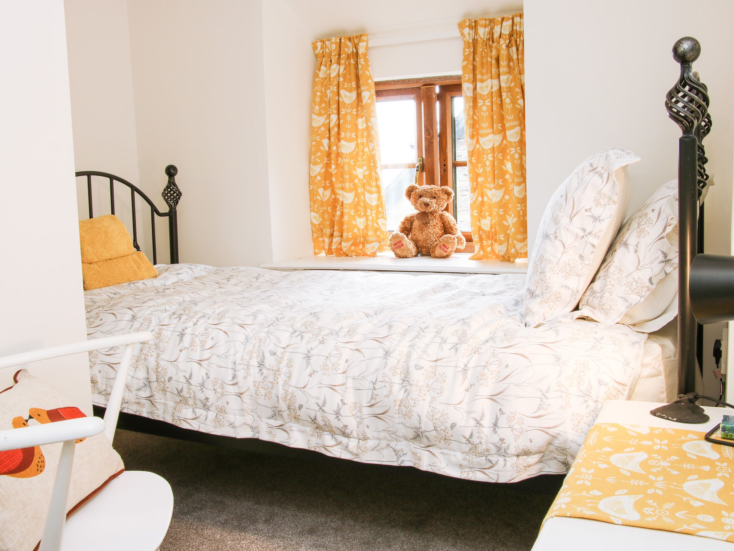 A bedroom with a bed, a window with curtains, a teddy bear, and a bedside lamp.
