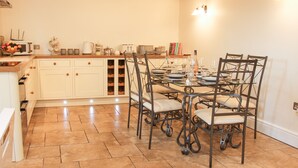 A dining area with a large table set for six, surrounded by six chairs. There is a kitchen area with white cabinets and a microwave on the counter. - Linley Lane Cottage (Bishops Castle)