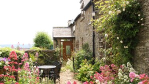 A garden with a table and chairs, a stone building, and a wooden door. - Linley Lane Cottage (Bishops Castle)