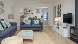 A modern living room with a sofa, ottoman, and a flat-screen TV. - 3 bedroom accommodation in Lympstone (Lympstone)