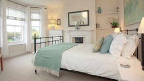 A bedroom with a bed, bedside table, lamp, fireplace, and a window with curtains. - 3 bedroom accommodation in Lympstone (Lympstone)