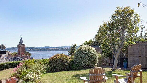 A grassy outdoor area with two wooden Adirondack chairs, a wooden shed, and a large bush. - 3 bedroom accommodation in Lympstone (Lympstone)