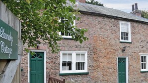 A brick cottage with a green door, a bench, and a sign reading 'Laundry Cottage.' - 3 bedroom accommodation in Rudston, near Bridlington (Rudston, near Bridlington)