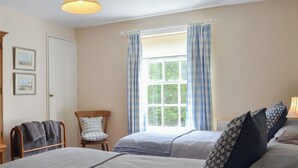A bedroom with two beds, a window with curtains, a chair, and a radiator. - 3 bedroom accommodation in Rudston, near Bridlington (Rudston, near Bridlington)