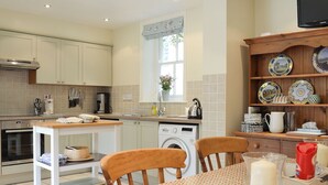 A kitchen with a washing machine, a dining table with chairs, and a shelf with decorative plates. - 3 bedroom accommodation in Rudston, near Bridlington (Rudston, near Bridlington)