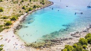 A coastal beach with clear turquoise waters, rocky shoreline, and sparse vegetation. - VILLA TANGO I (Okrug Gornji)