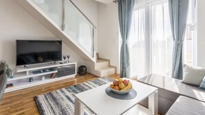 A modern living room with a flat-screen TV, a staircase, a dining area with a fruit bowl, and a sofa. - VILLA TANGO I (Okrug Gornji)