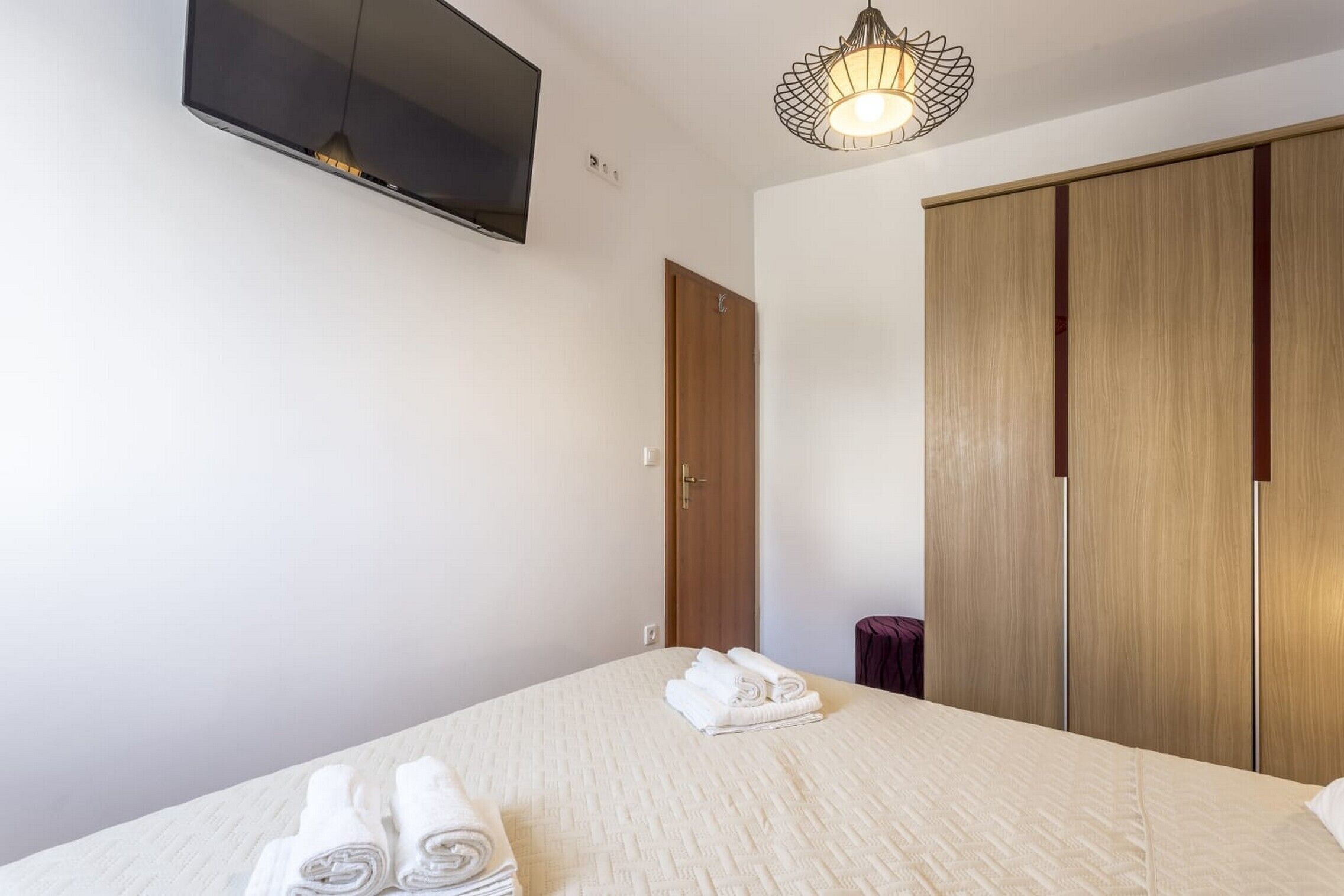Une chambre d’hôtel comprenant un lit, un téléviseur fixé au mur, une armoire et une table de chevet avec une lampe.