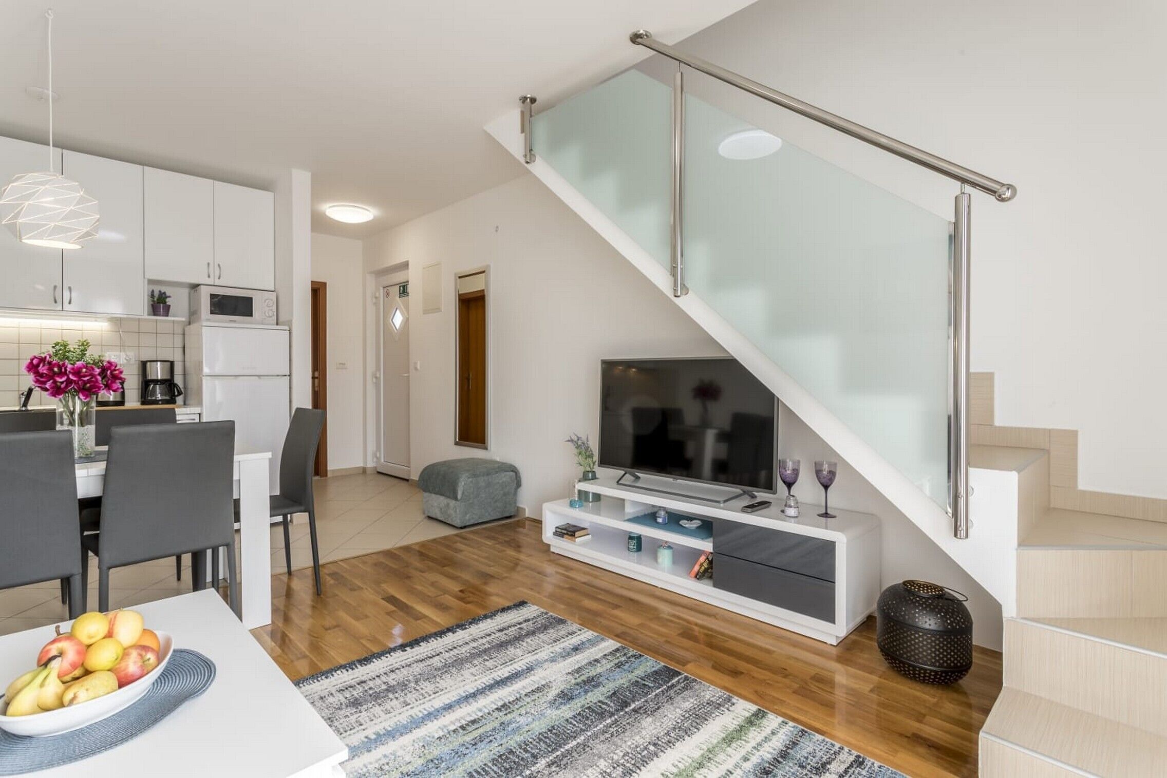 Un salon moderne avec un escalier, un coin repas et une cuisine.