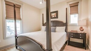 A four-poster bed with a headboard, a bedside table with a lamp, and a window with blinds. - Enjoy Life at River Rocks Plantation (Guntersville)