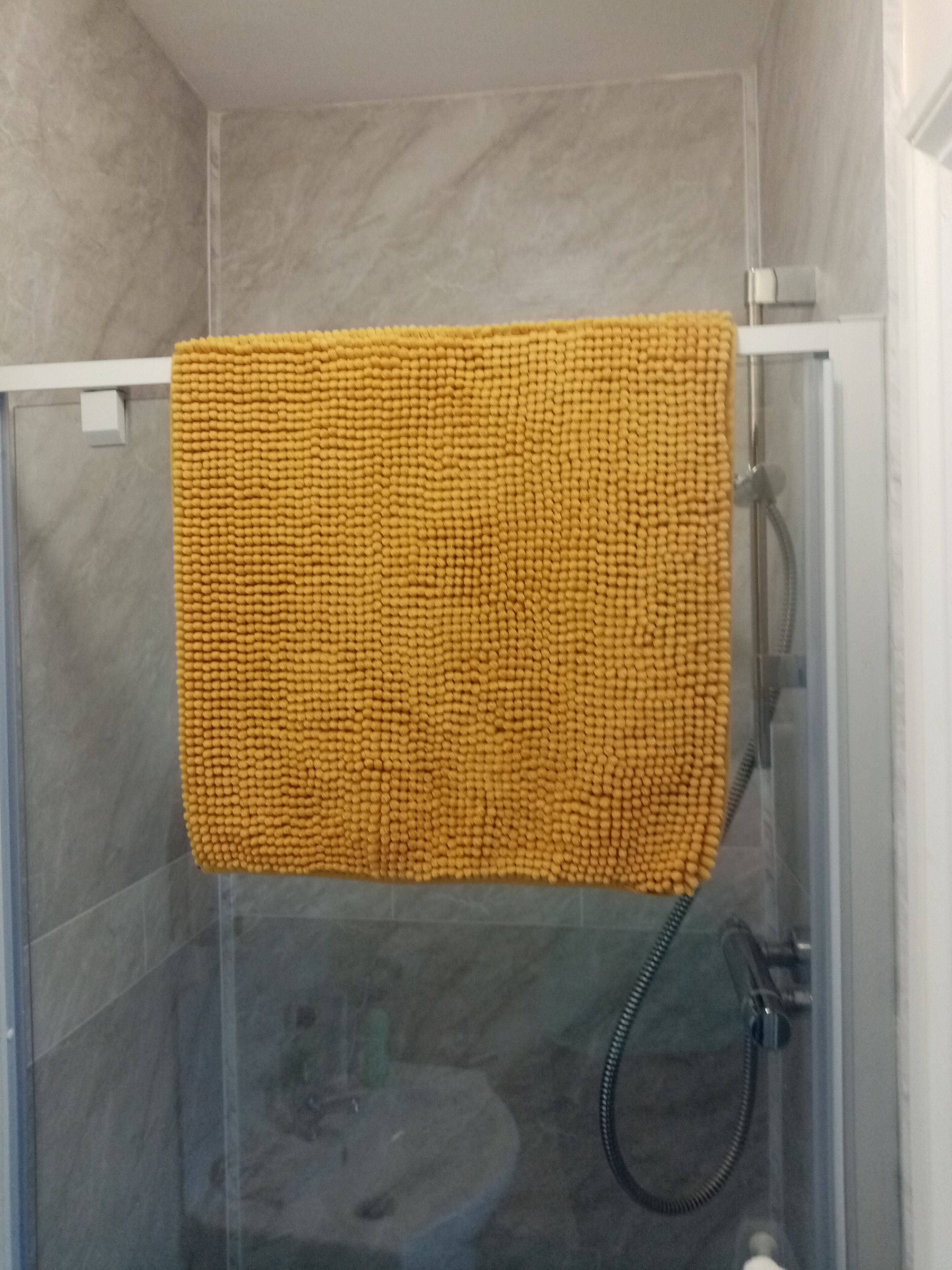 A glass-enclosed shower stall with a yellow textured towel hanging on the door.