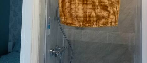 A shower area with a clear glass door, a yellow textured bath mat, and a wall-mounted soap dispenser.