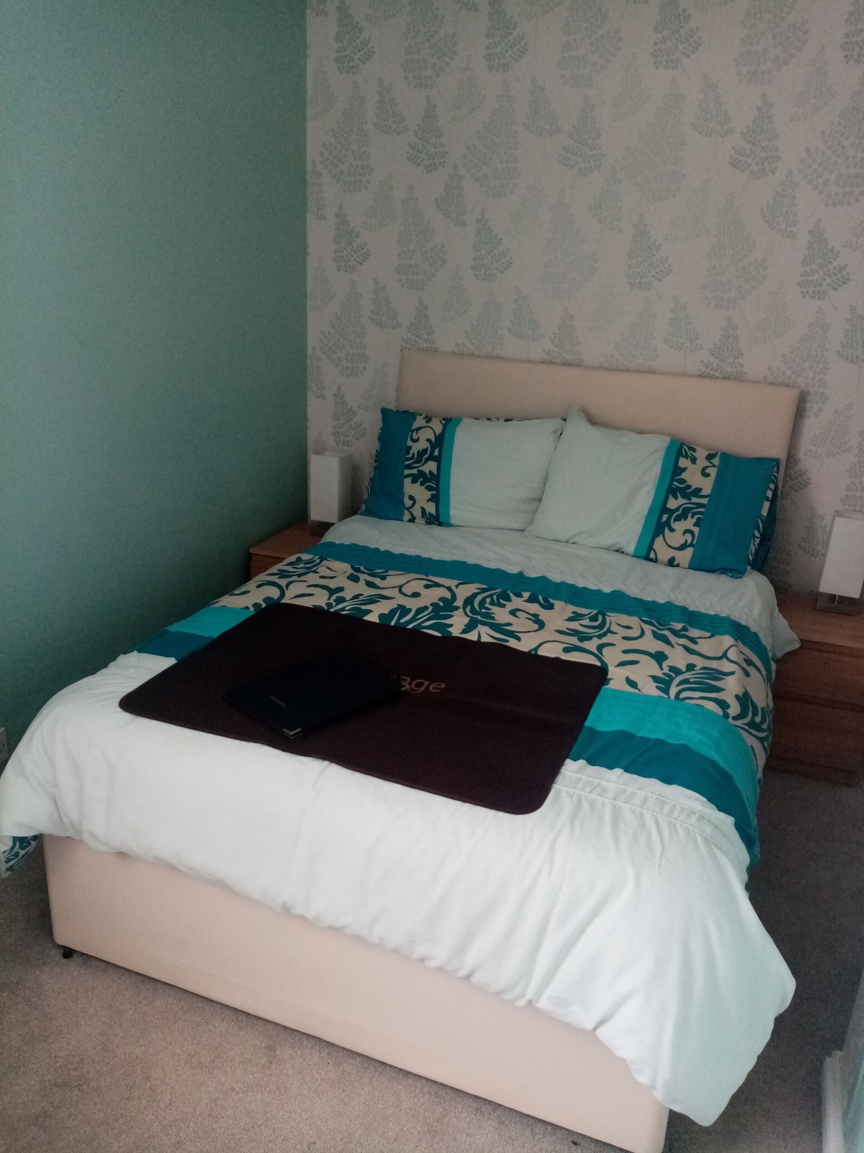 A bed with a patterned bedspread, a pillow with a blue and white design, and a black object on the bed.
