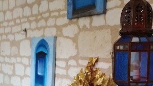 Une pièce avec un mur en pierre, une console blanche agrémentée d’objets décoratifs, une porte bleue et une lanterne traditionnelle.