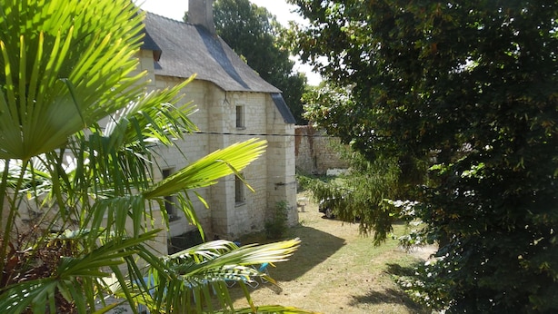 Un bâtiment en pierre doté d’un toit en pente, entouré d’arbres et d’une zone herbeuse.