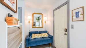 A hallway with a blue sofa, a wooden cabinet, a mirror, and a white door. - French Toast Flat (Moscow)