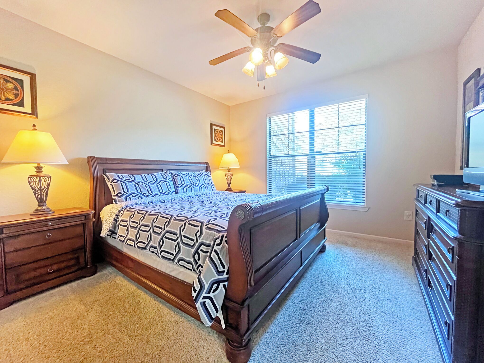 A bedroom with a bed, nightstands, a dresser, a ceiling fan, and a window with blinds.