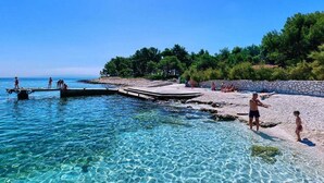 Une plage à l’eau claire, une jetée et des gens sur le rivage.