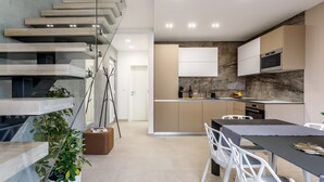 Une cuisine moderne avec un pare-feu en marbre, un coin repas avec des chaises blanches et un escalier doté de rampes en verre.